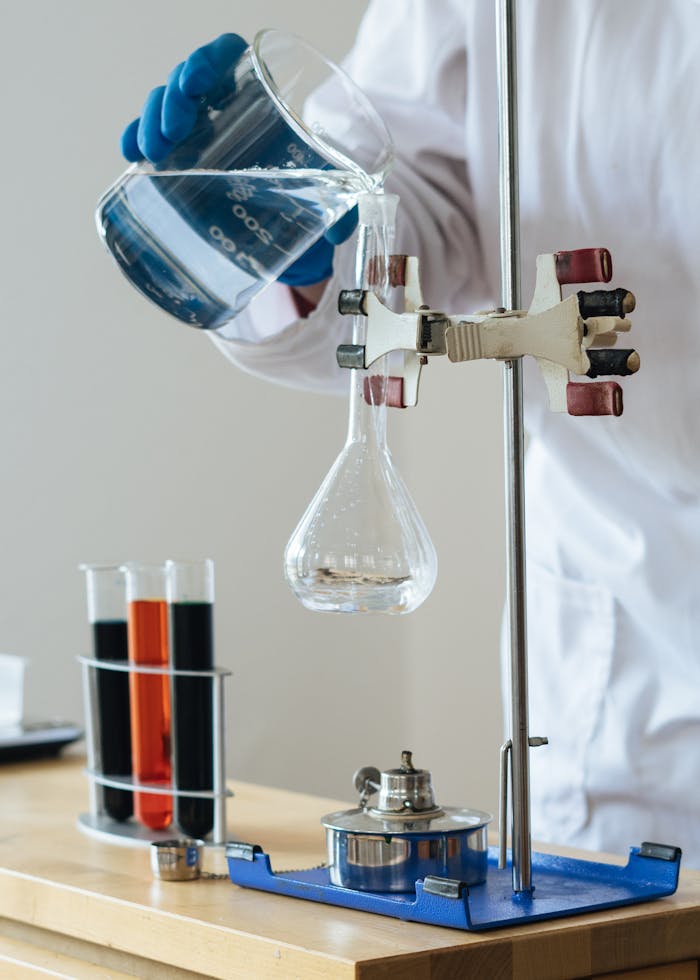 Crop chemist pouring clear liquid into fragile glassware in science center